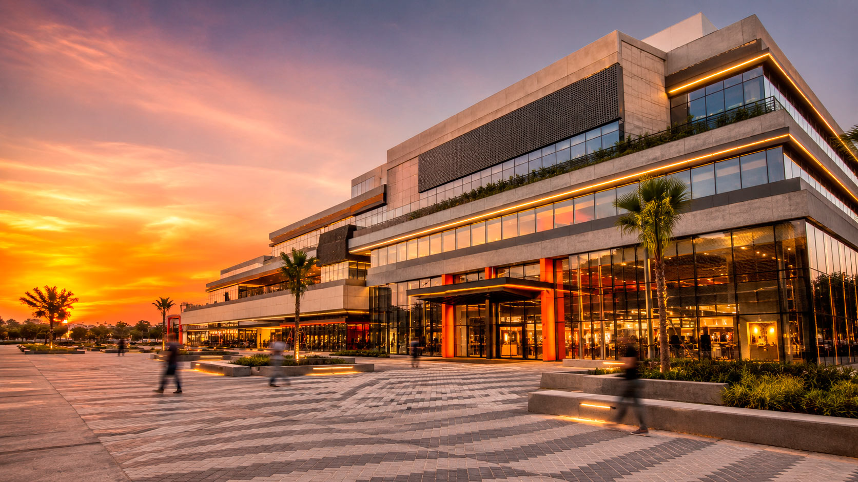 IMAGEN HERO — PLAZA COMERCIAL MODERNA AL ATARDECER: Fotografía arquitectónica panorámica de una plaza comercial contemporánea de gran escala, vista en perspectiva diagonal de abajo hacia arriba. Edificio de 5 a 6 niveles con fachada de líneas limpias combinando hormigón visto color gris claro, paneles metálicos perforados color grafito y amplios muros cortina de vidrio. Acentos arquitectónicos en naranja vibrante en marquesinas y señalética. Explanada frontal con piso de adoquín de concreto en patrón geométrico, jardineras lineales con vegetación verde, bancas de diseño minimalista. Iluminación de hora dorada (atardecer) con luces LED cálidas ya encendidas en interiores y franjas LED en cornisas. Personas caminando difuminadas por movimiento. Cielo despejado con degradado naranja-ámbar. Estilo: fotografía profesional de arquitectura comercial, ultra realista, 4K, gran angular, alto contraste y colores saturados vivos.
